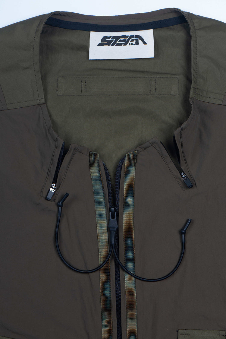 CLERIC utility nylon vest in vine gray green — close-up of the split zip neckline, drawcord and STEAM neck label