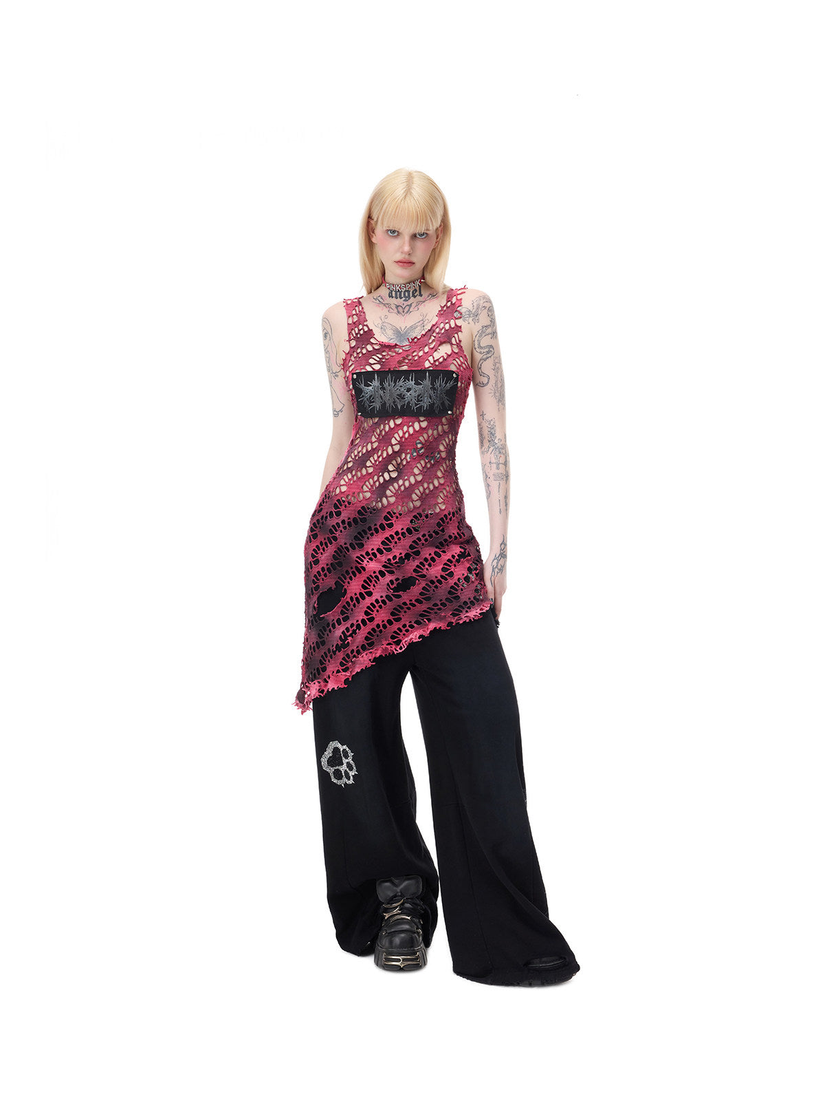 PINKSPINK AFTERGLOW distressed open-knit asymmetric dress in hot pink — angled full-length front modeled view showing the diagonal hem over separate black trousers