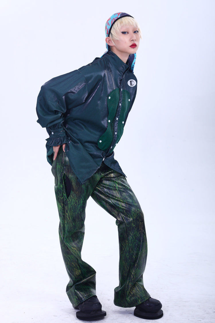 EMBRYO TRIANGLE ARMOR lace-inset leather pants in green — full-length modeled outfit with green overshirt and patterned cycling cap