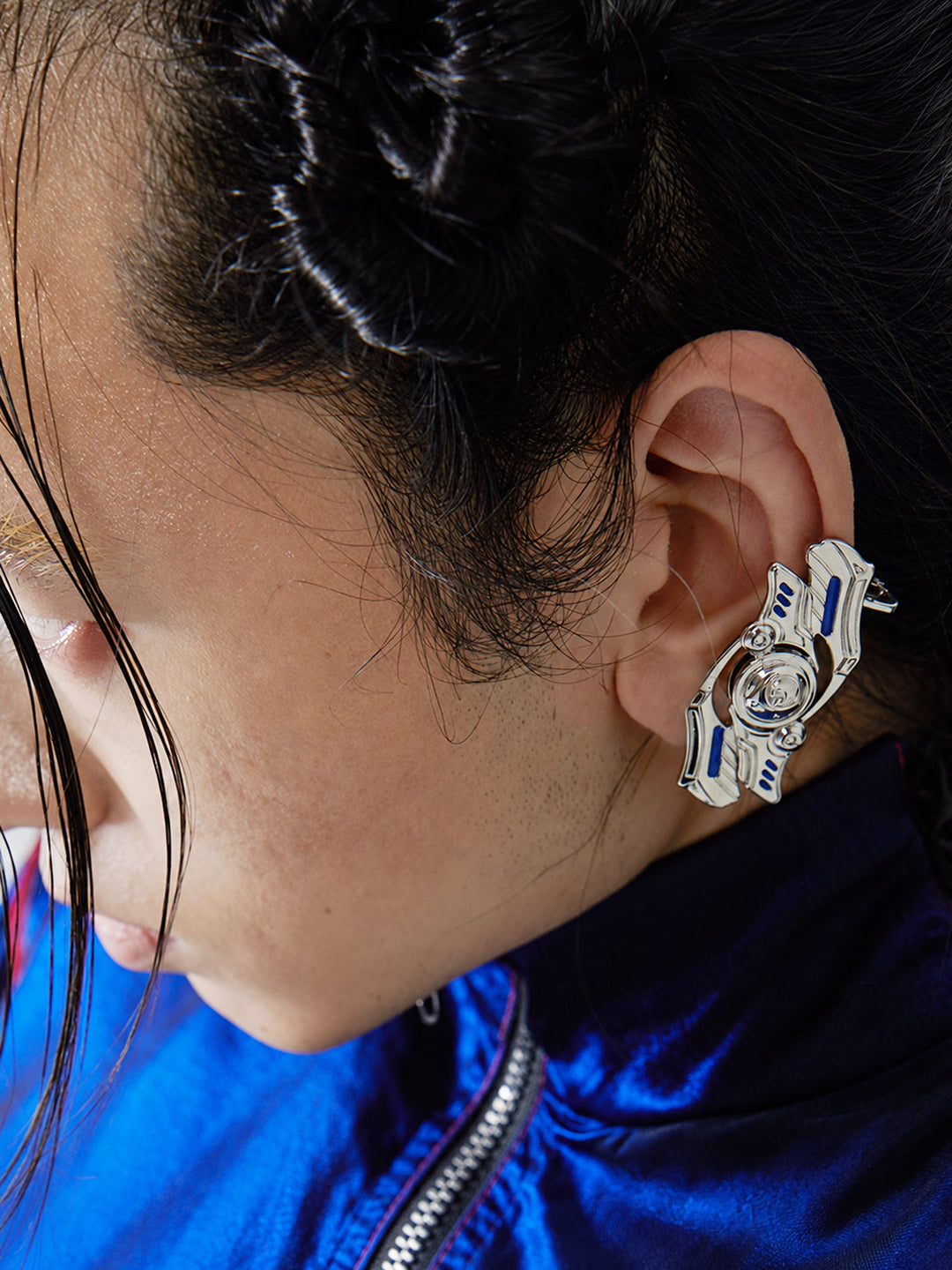 EMBRYO CURSE rotating cyber earrings — modeled ear close-up showing silver mechanical plates, blue inlays and rotating center
