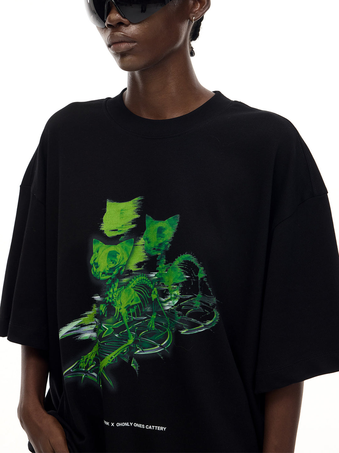 PINKSPINK MONSTER cat-skeleton oversized graphic tee in black — close-up of the green cat heads and skeleton print on the chest