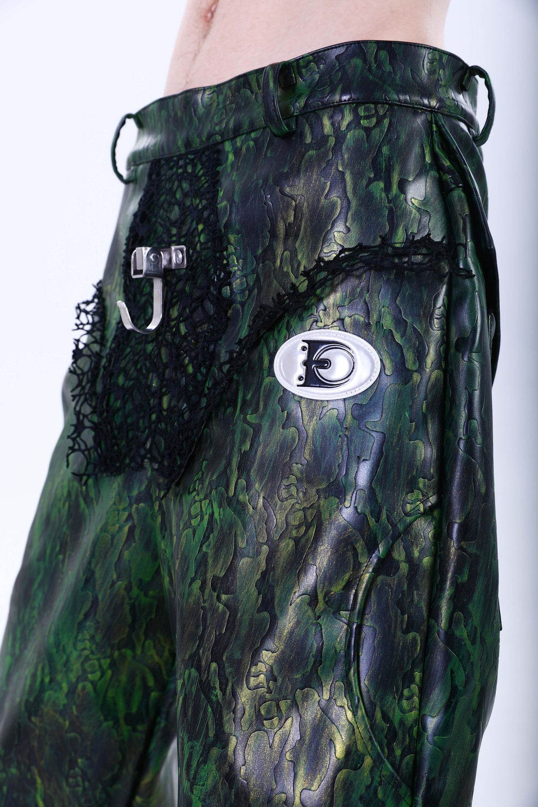 EMBRYO TRIANGLE ARMOR lace-inset leather pants in green — front waist close-up showing black lace inserts, metal clasp and oval logo plaque