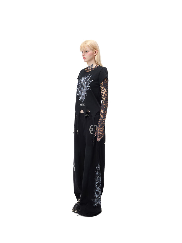 PINKSPINK PUNK CACTUS studded pointed-hem tee in black — full-length side modeled view over a separate leopard mesh layer and black trousers