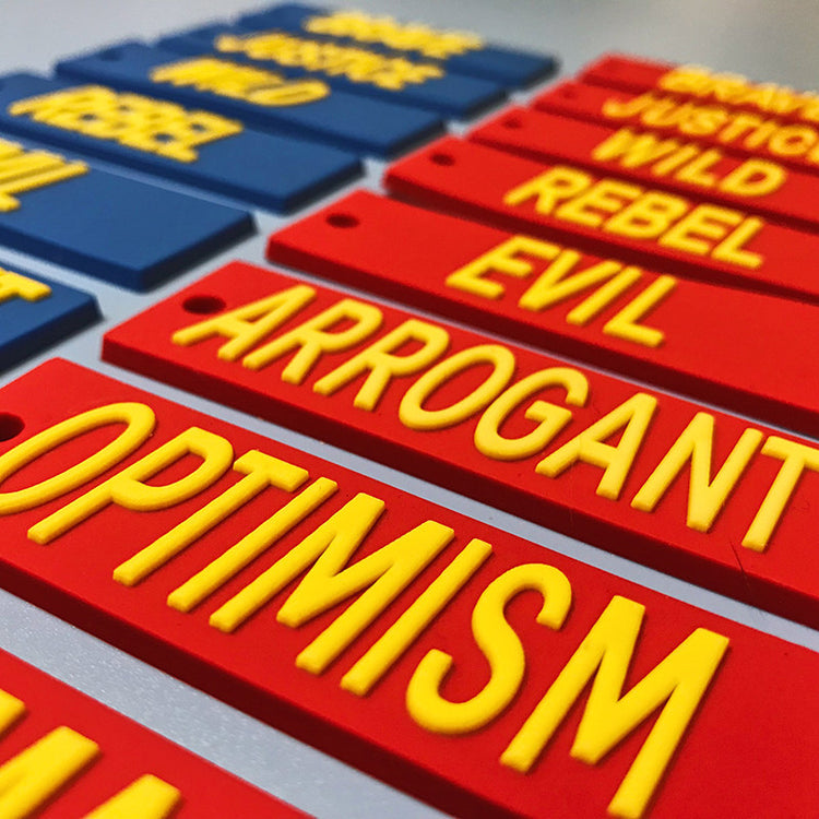 EOH-STUDIO BTBM raised yellow ARROGANT and OPTIMISM lettering on red silicone earring panels, low-angle construction detail.