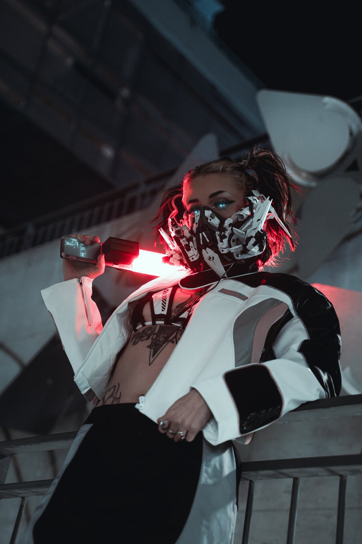 Masked figure in a white and black motorcycle jacket holding a red light against an architectural city backdrop. Photography by Dylan Newton.