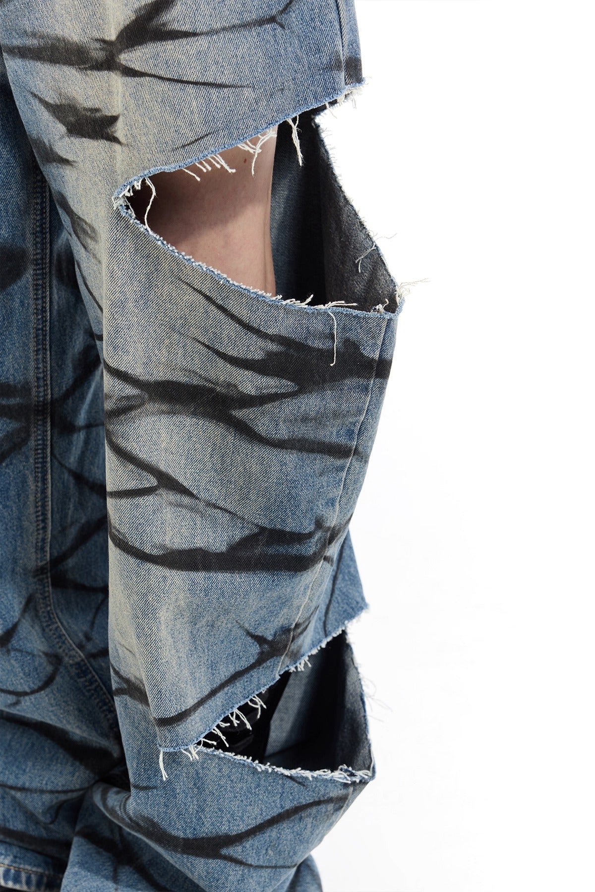 PINKSPINK REMAKE layered graffiti low-rise jeans in washed blue denim — close-up of raw-edged thigh cutout and black graffiti marks.