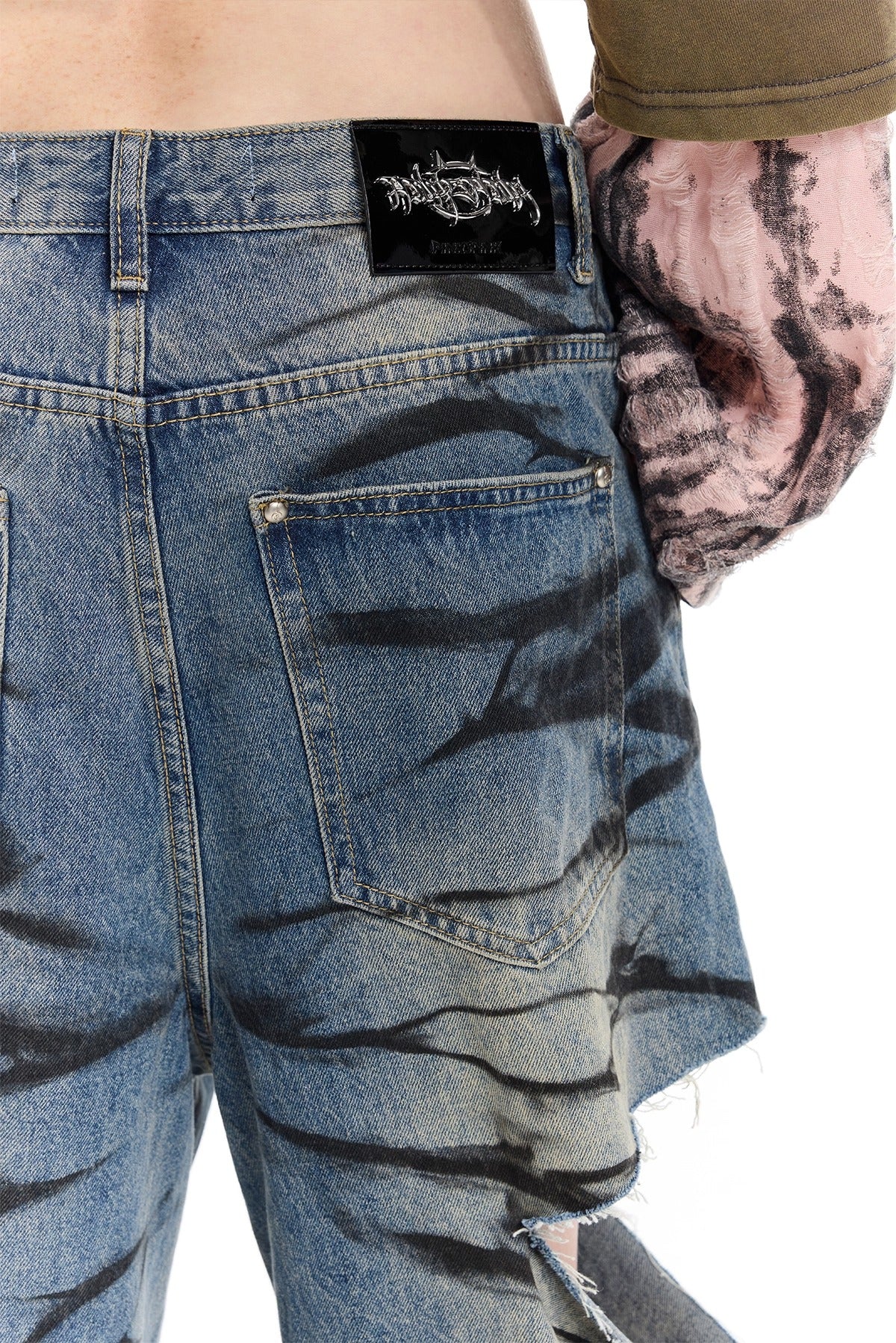 PINKSPINK REMAKE layered graffiti low-rise jeans in washed blue denim — close-up of a rear patch pocket and photographed brand label.
