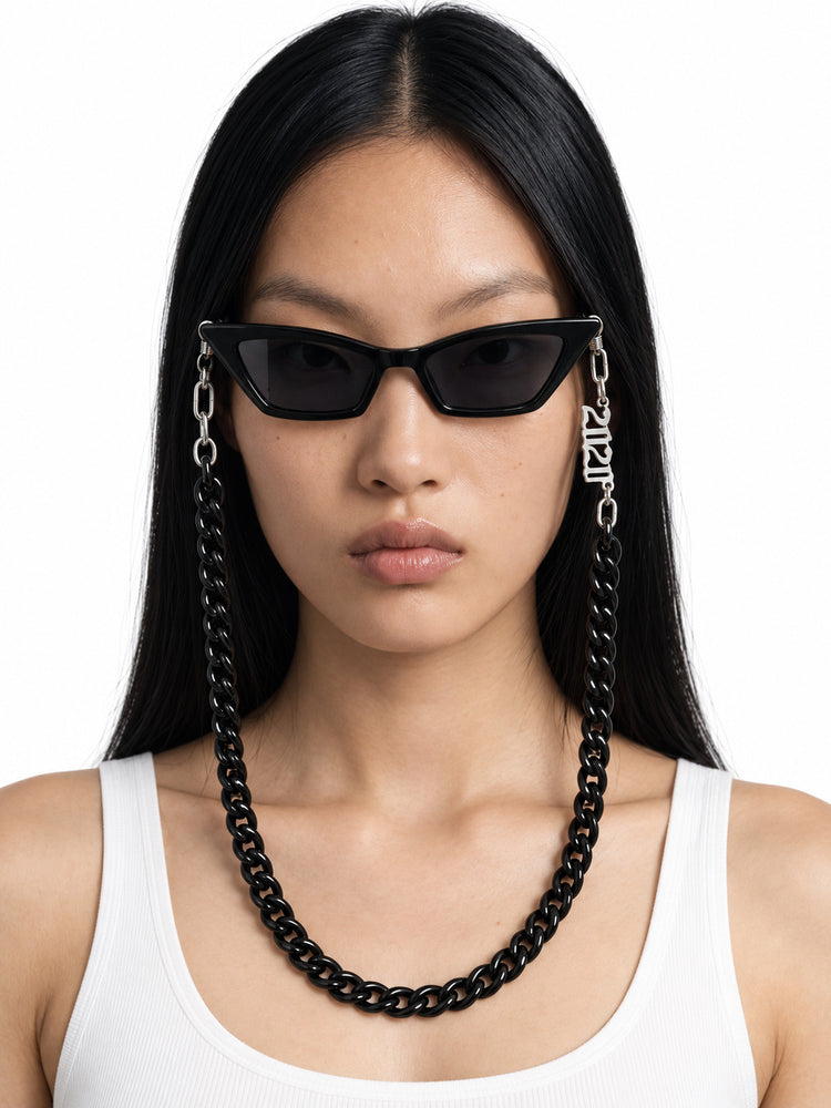 RICH BABY black cat-eye sunglasses with the included black chain, worn by Chell in a front studio portrait