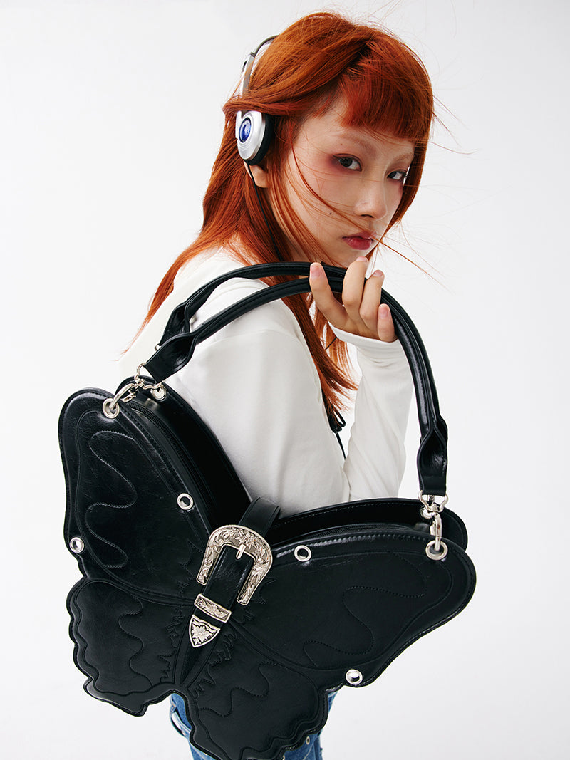 CIGABERRY butterfly-shaped faux-leather bag — black large bag lifted over the shoulder with a white outfit, close view.