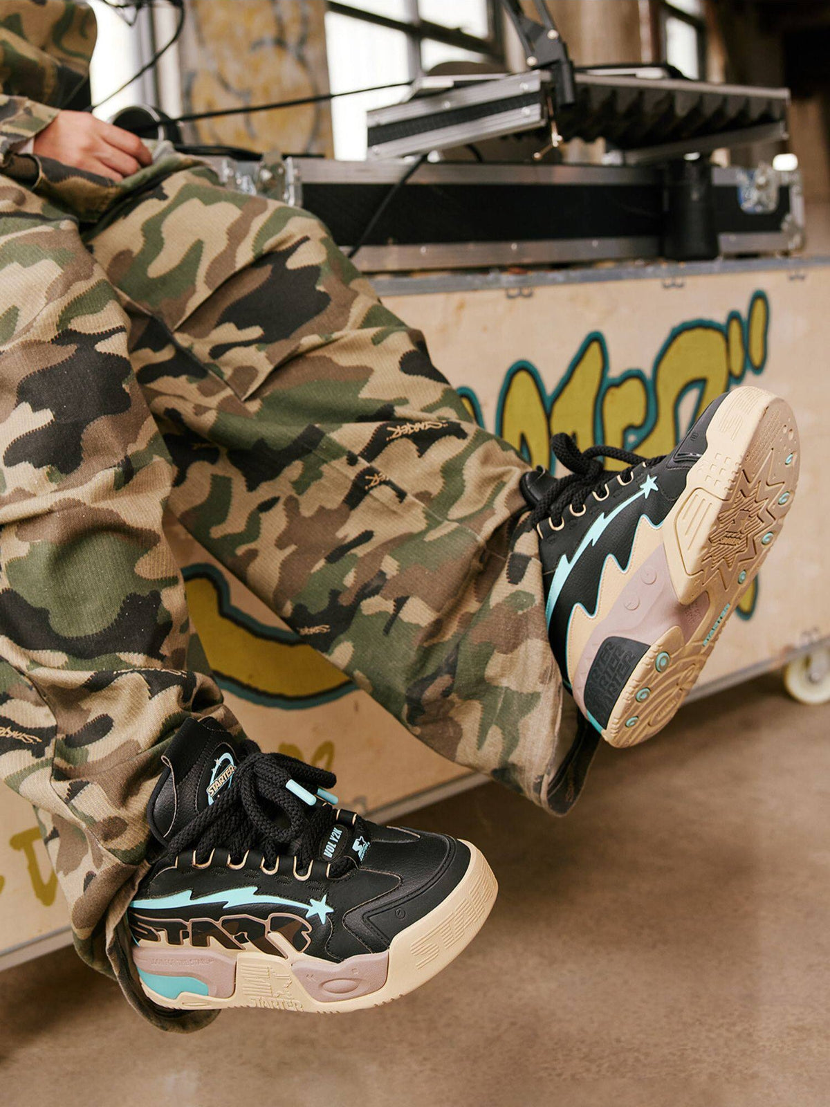 Black STARTER platform sneakers with blue accents worn with camouflage trousers, side and outsole view