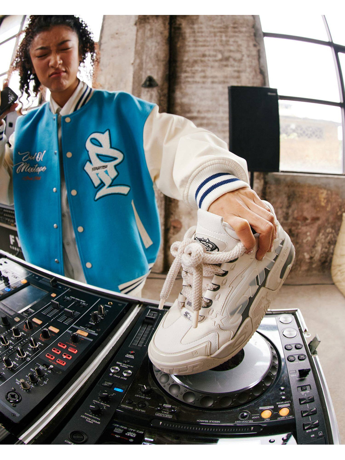 White STARTER platform sneaker held above DJ decks by a model in a blue varsity jacket