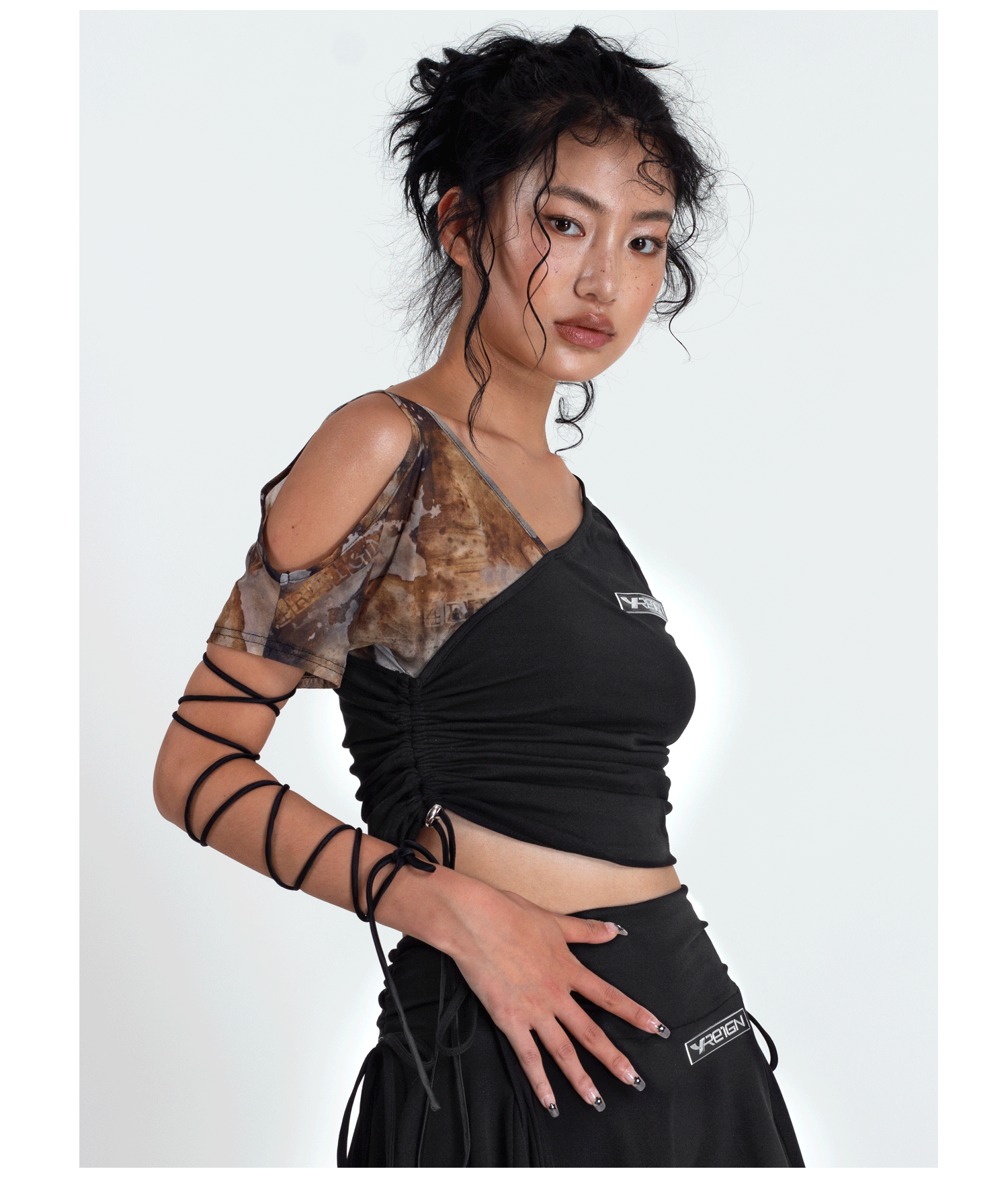 4RE1GN TIE-DYE SLEEVE asymmetric crop top, side-front pose with the tied arm raised