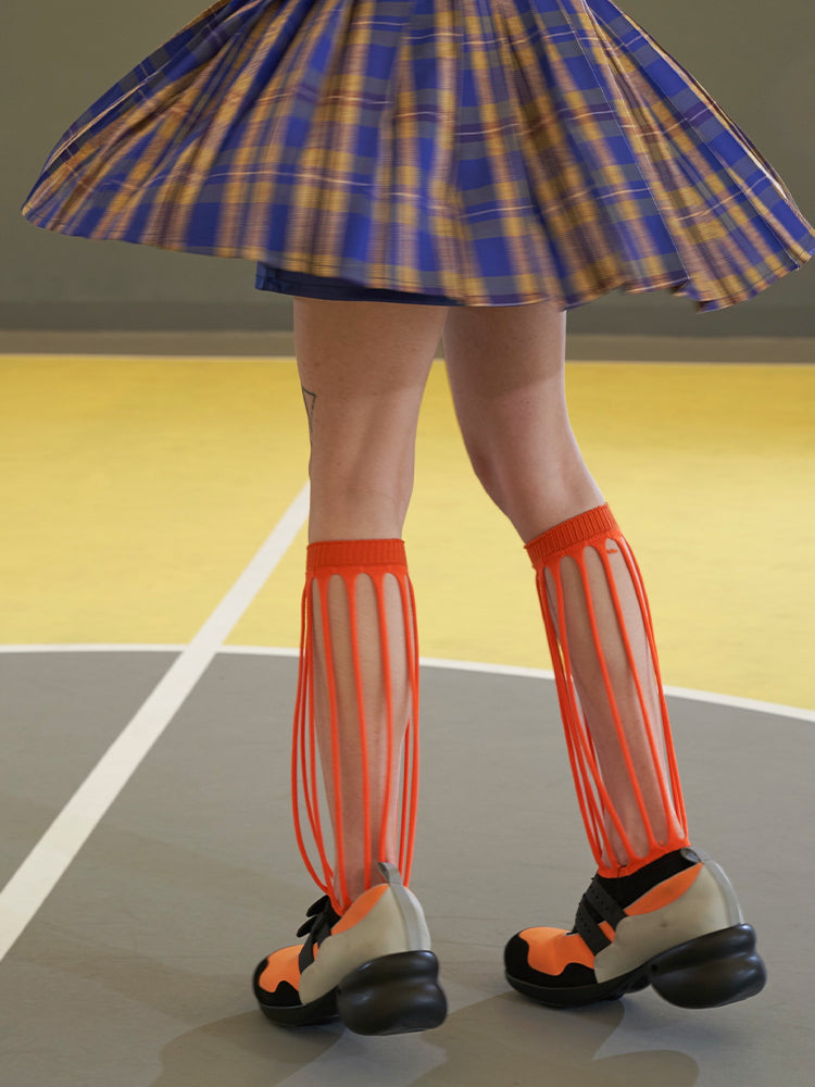 NEXT PASSPORT MULTIPASS cutout knee-high socks — orange cutout socks in a rear three-quarter view beneath a plaid skirt.